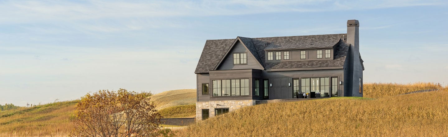 dark gray home with black framed Andersen windows and doors surround by wheat fields