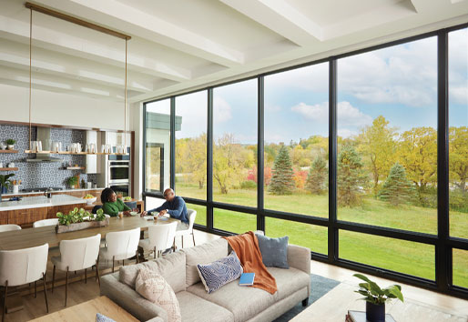A window wall created by picture windows with awning windows underneath floods a living room with natural light and showcases views of a green lawn and trees outside.
