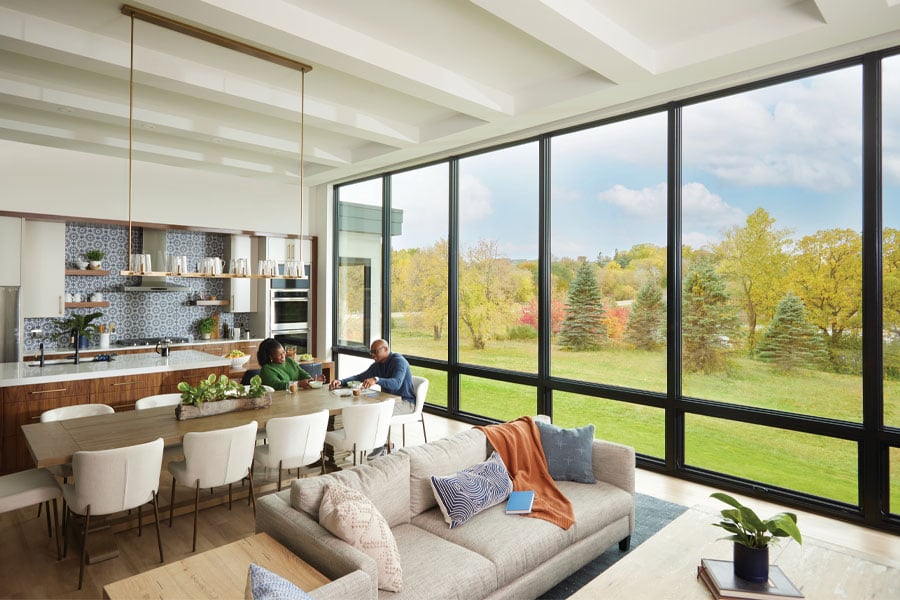 A window wall created by picture windows with awning windows underneath floods a living room with natural light and showcases views of a green lawn and trees outside.