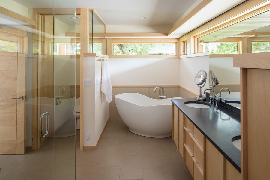 Clerestory windows bring natural light into a bathroom that features a large soaking tub and light-colored maple wood windows, trim, and cabinetry.