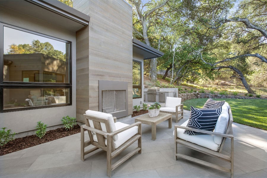 A patio with an outdoor fireplace next to a contemporary home with large windows. 