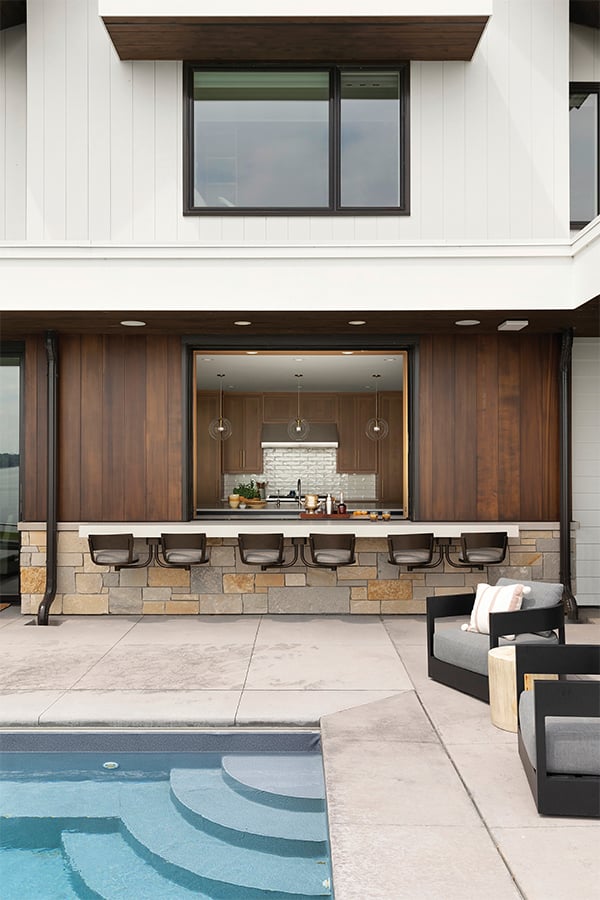 An open pass-through window connects a kitchen with a concrete patio and outdoor pool.