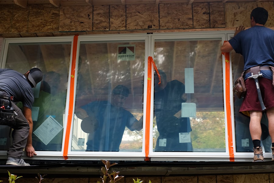 An exterior shot of five men installing a row of new windows. 