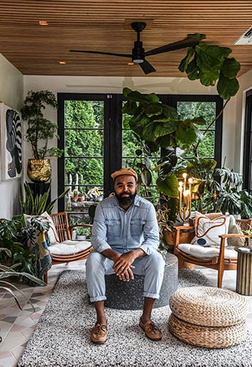 Hilton Carter sitting in open-concept sunroom with plants and folding black door