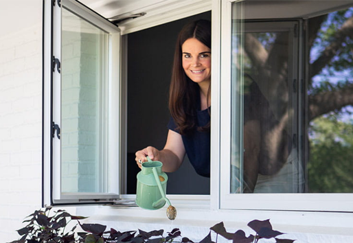  Michelle Adams waters plants in her window box out of an open andersen casement window