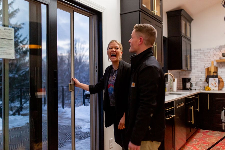 A woman tries out her new black-framed sliding patio door while a contractor stands by. 