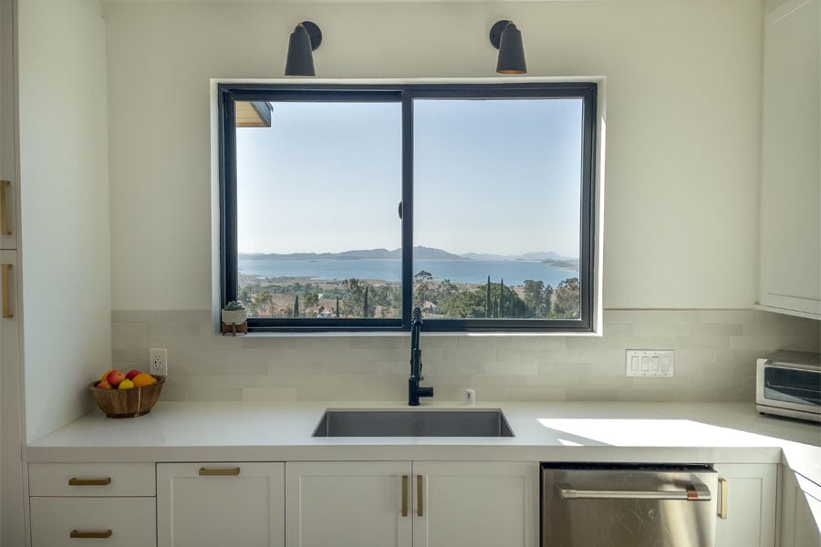 A gliding window above a kitchen sink frames a view of a lake and mountains beyond.