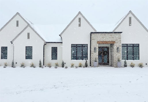 A white home with new black windows is snug against the snowy, cold landscape outside. 