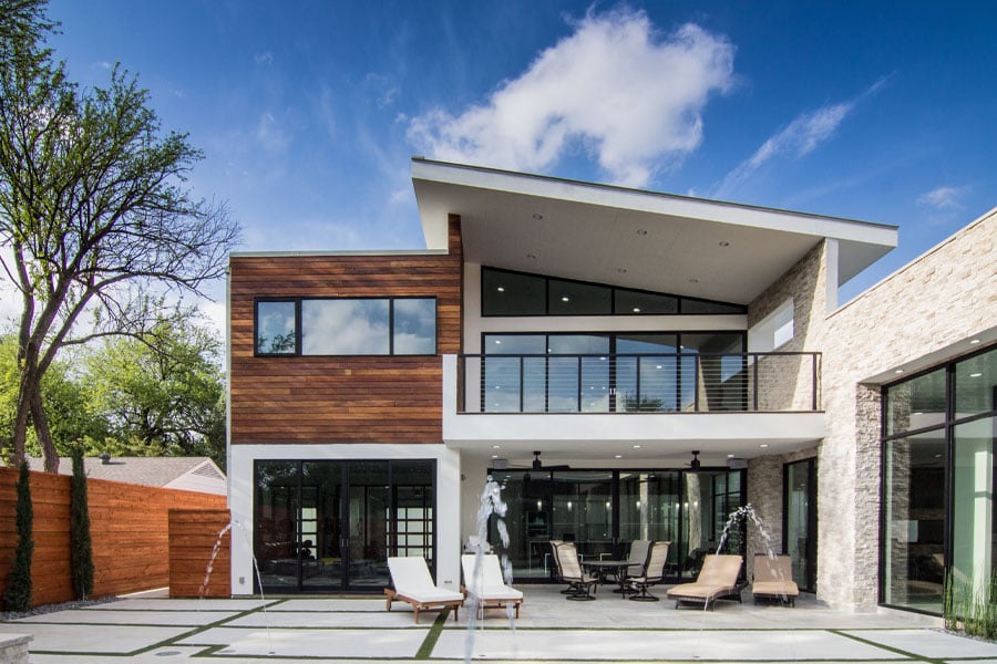 An exterior view of a white and wood modern home with lots of windows and doors facing the swimming pool.