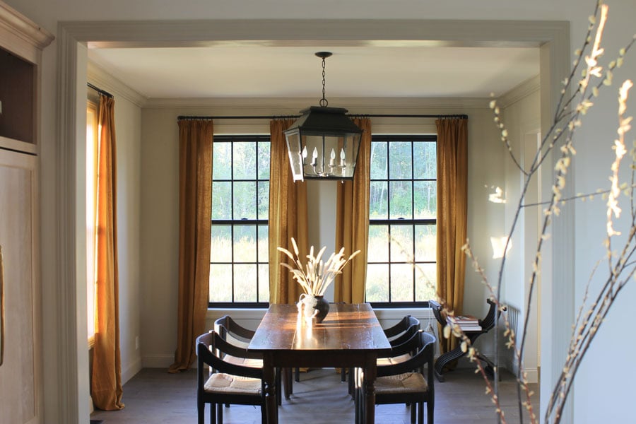 A dining table with lantern above and black-framed single-hung windows behind 