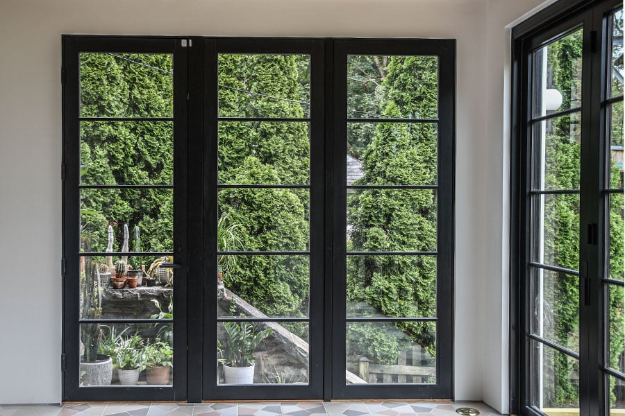 A black-framed hinged door and two floor-to-ceiling windows next to it create a full wall of glass matching a bi-folding door on the adjacent wall.