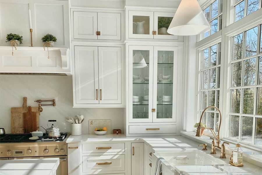 Light streams into an all-white kitchen through sparkling clean windows.