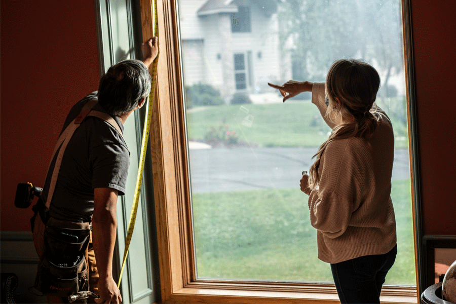 A contractor measures a window while talking with a homeowner.