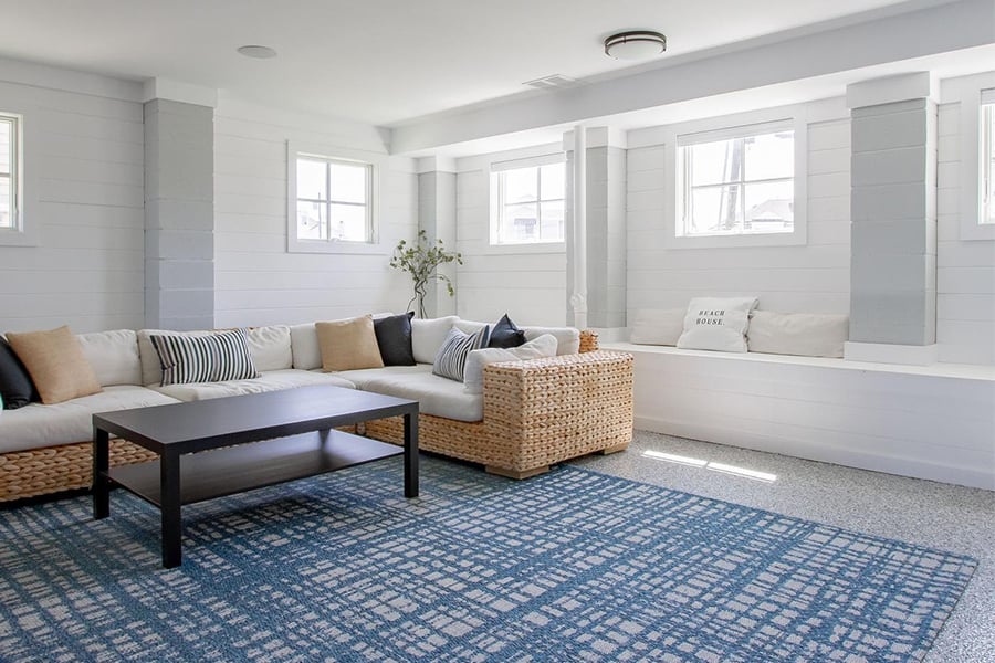 A basement living room with windows along two walls, a window seat, couch, coffee table, and blue rug.
