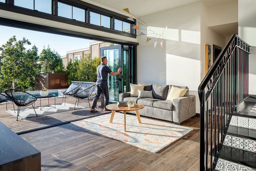 A man pushes open a bi-folding door connecting a family room to a deck outside. 