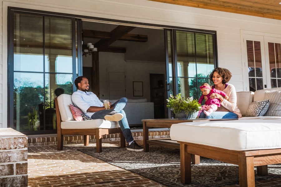 A couple and their baby relax on a patio in front of a sliding glass door. 