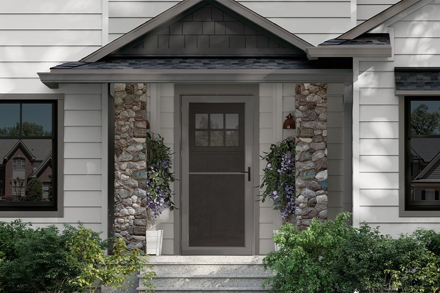 An exterior view of a home with white siding, stone pillars next to the front door, and a charcoal gray storm door.
