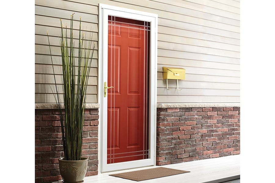 An exterior view of a home’s entryway with beige siding, brick trim, and a bright red front door with a Fullview Interchangeable Storm Door installed over it.