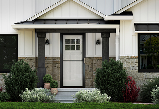 An exterior view of a home’s entryway showing its white siding, black windows, landscaping around the front door, and a black storm door over a white front door.