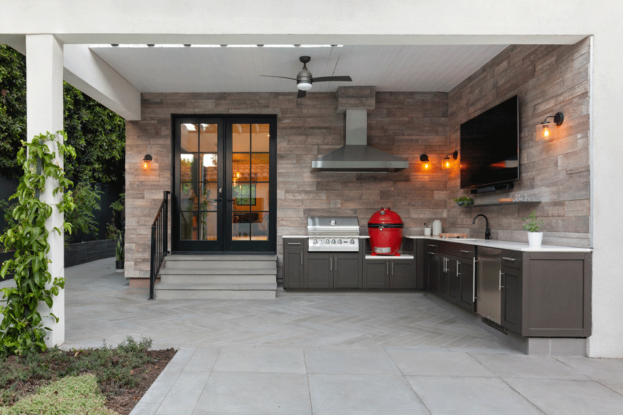 An outdoor kitchen featuring cabinetry, grill, smoker, sink, and a big-screen TV connects to the indoor kitchen through a set of Andersen French doors.