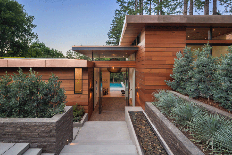 A modern home with cedar cladding features all-glass double pivot doors at the entrance.