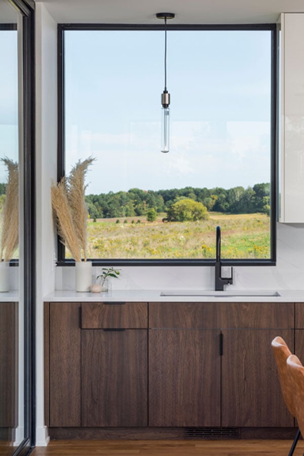A kitchen sink with a picture window above it frames an expansive view of rolling prairie. 