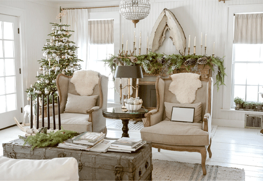 A living room decorated with a Christmas tree, cozy fur throws, and a mantle covered in greenery, pinecones, and candles. 