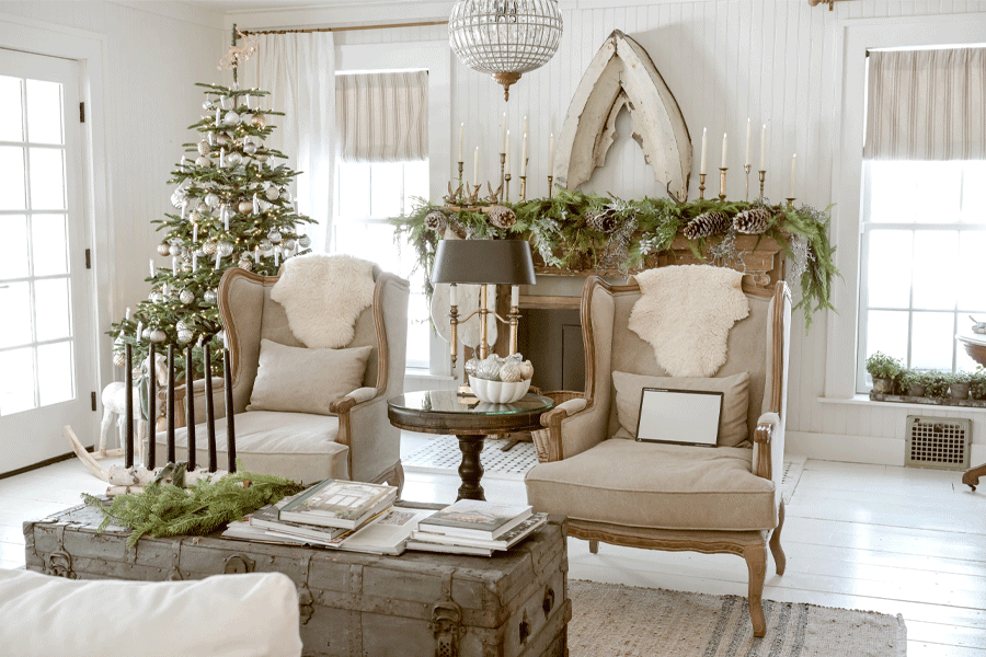 A living room decorated with a Christmas tree, cozy fur throws, and a mantle covered in greenery, pinecones, and candles. 