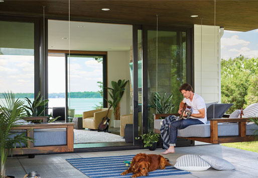  Man plays guitar while sitting on a swinging porch bed with golden retriever at his feet