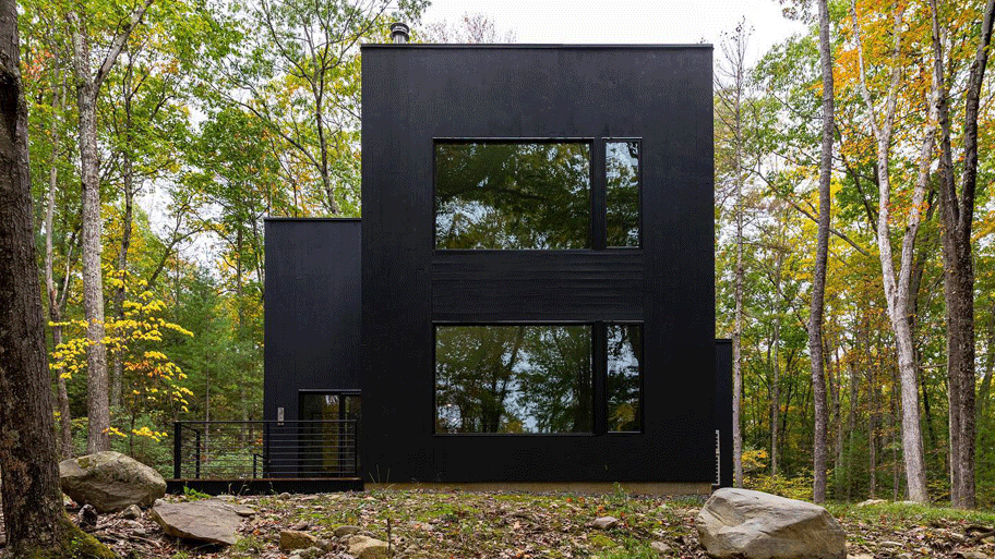 A modern black home with oversized windows stands out against its wooded lot.