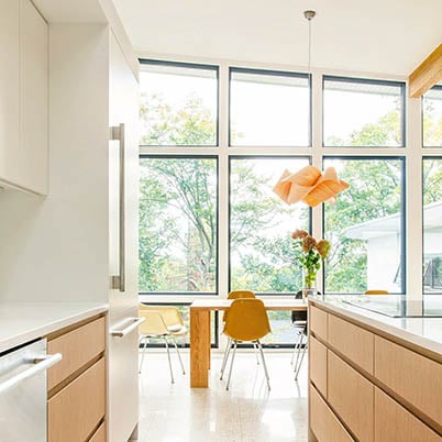 White kitchen with brown cupboards and large Andersen Windows showcasing the outdoors allowing in natural sunlight to create a healthy home environment