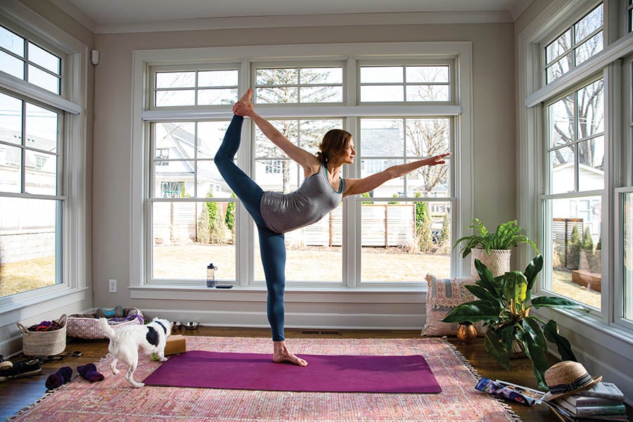 Person doing yoga in front of white Andersen 400 Series Tilt-Wash Double-Hung windows with 2x2 grilles in the upper sash 