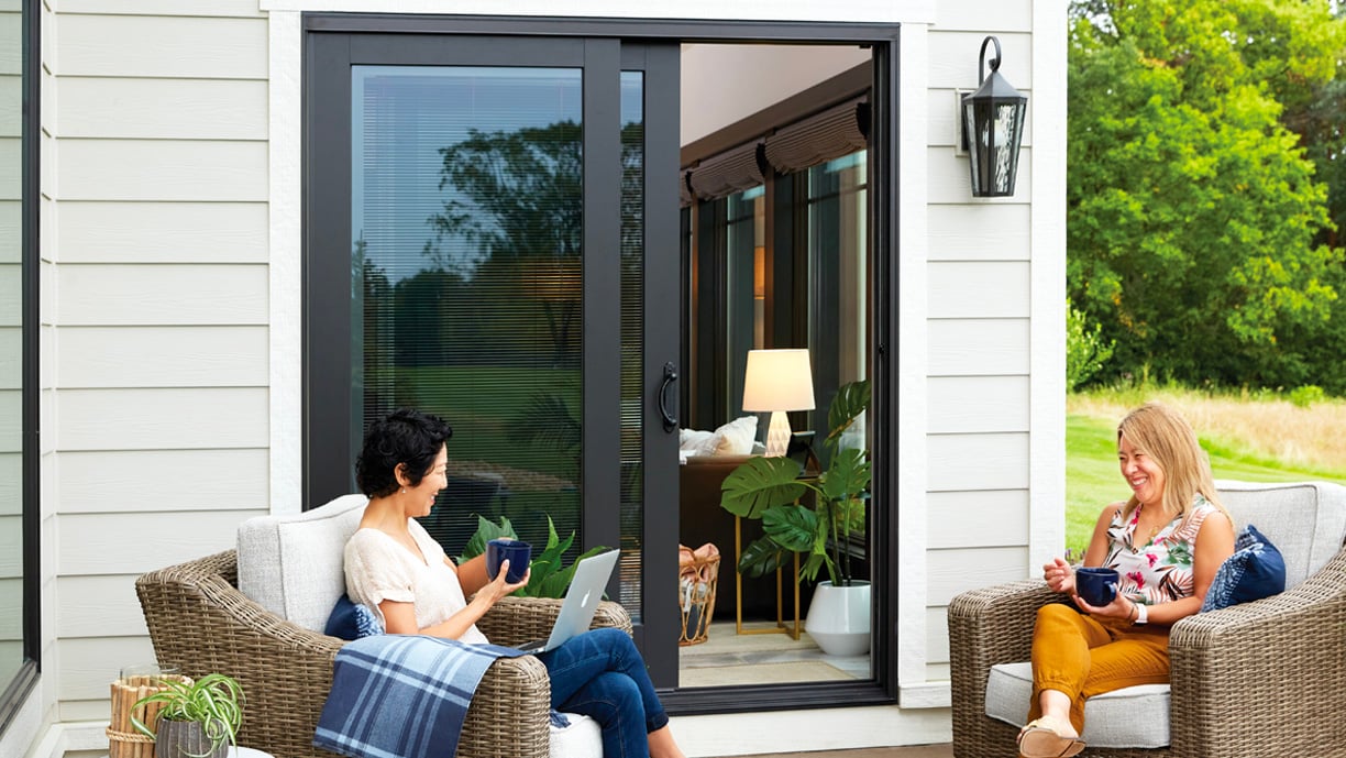 man and woman sitting on patio in front of andersen gliding patio doors