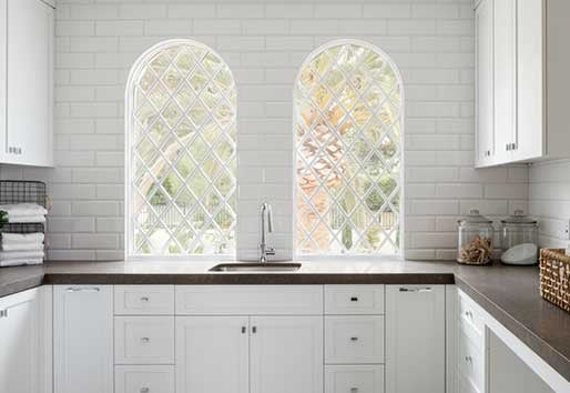 White kitchen with Andersen e-series specialty windows with diamond grilles above the kitchen sink.